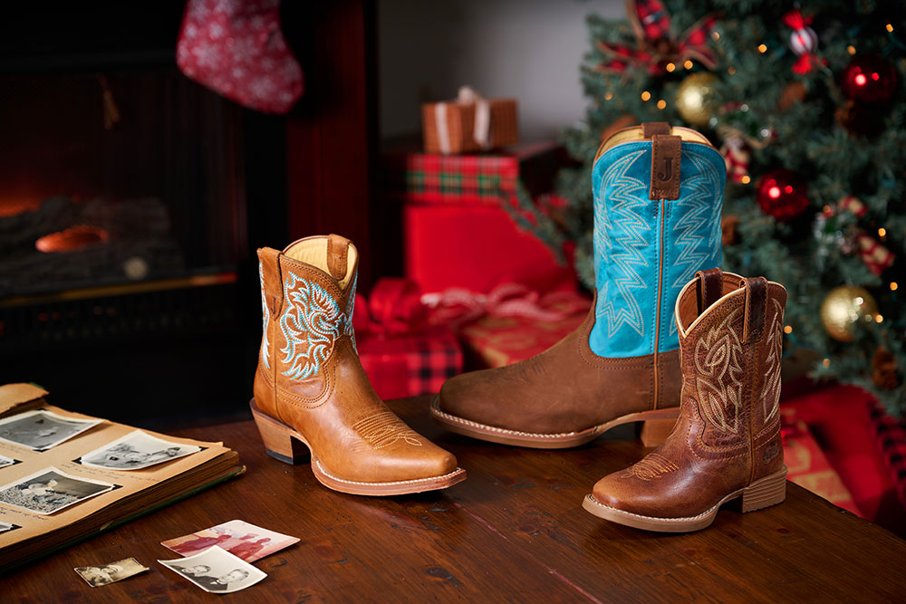 Canter Junior in Amber Brown, Jackpot 11" Western in brown, and Isabella 7” in tan cowboy boots posed on a table with a Christmas scene behind them.